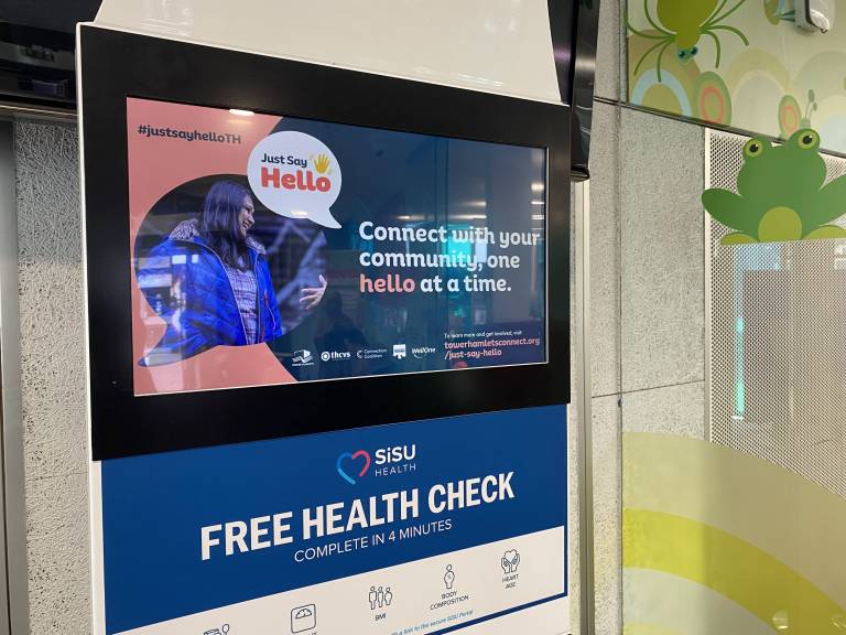 A health check kiosk showing a Just Say Hello poster on the screen