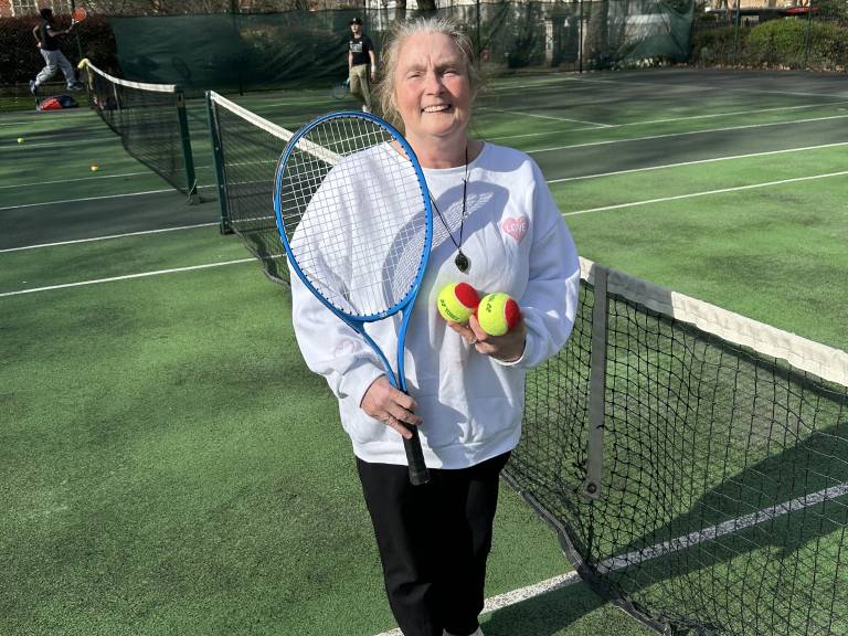 A woman attending the Community Tennis for Health over 50's session poses for a photo near the net